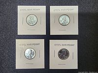 Four 1943 steel pennies in individual holders labeled 'STEEL WAR PENNY' showing obverse side with Abraham Lincoln profile.