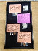 Top-down image showing five assorted coins in a presentation case, each with historical info cards about Lincoln Head Cents and Eisenhower Dollar.