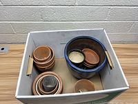 Top view of lot of assorted flower pots including terracotta and blue ceramic pots in a cardboard box.