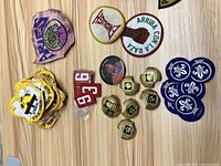 Top view showing assortment of patches and pins including Avery patch, green and white peace patches, blue Scout patches, yellow Bike Fair patches, red number '93' patches, hexagonal gold-tone pins, and circular photo pin.
