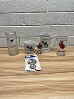Front view of the lot showing assorted Cardinals football drinkware, figurine, and button pack arranged in a row on a light wood surface against a gray wall.
