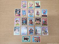 Top-down view of 20 original Garbage Pail Kids cards laid out in 4 rows on a wooden surface, showing colorful illustrated characters with names at the bottom.