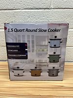 Photo of the product box showing 1.5 Quart Round Slow Cooker and listing features such as removable pot, included lid, and removable stoneware.