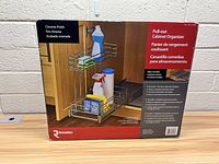 Front of the box showing product name, usage scenario with cleaning supplies in organizer, chrome finish indicated