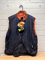 Front view of the black side of the new Remington vest hanging on hook with tags attached