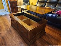 Photo showing the coffee table with the lift top open revealing two internal storage compartments and six drawers on the front.