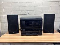 Complete stereo system with two speakers on either side placed on wooden surface against white brick wall