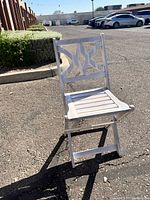 White wooden folding chair shown outdoors from the front with shadows visible on ground