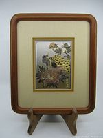 Full view of chokin art piece with teak wood frame on stand showing peacock and floral motifs