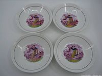 Overhead view of four white porcelain bowls showing central hand painted and transfer printed image of a woman and child in a pastoral scene with pink flowers and purple sky, each bowl with thin rim line