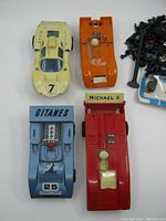 Top-down view showing four 1/32 scale race cars: two Strombeckers (yellow and orange), one red Strombecker, and one blue Polistil, alongside some parts.