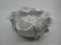 Front angled view of white porcelain lotus-shaped bowl with flower frog in center and detailed lotus petals and buds on rim.