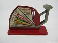 Side view of red and silver Jiffy-Way egg scale with measurement dial showing egg size classification and weight.
