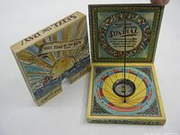 Closed view of the maritime pocket sundial showing the outer illustrated cover with a ship, sea waves, and a scroll banner saying 'Tell Time by the Sun'.