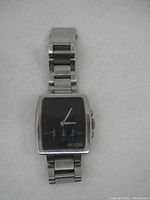 Front view of Nixon wristwatch showing square black dial with white and blue hands and Nixon logo.