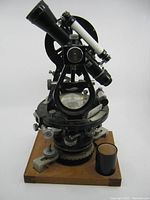 Front view of the 5 inch surveyors transit instrument showing telescope, adjustment knobs, circular scales and wooden base.