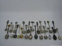 Front view of 24 vintage souvenir spoons laid out in a single row showing various sizes and handle designs.