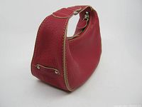 Side view of the red leather clutch purse showing shape, handle, and cream trim.