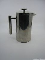 Full frontal view of the stainless steel French press showing handle, lid with plunger knob, and the spout outward.