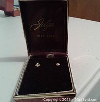 Pair of 14K yellow gold flower stud earrings displayed inside a Jolyn branded jewelry box with black velvet interior and burgundy lining.