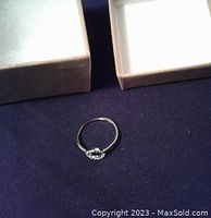 Sterling silver halo ring placed on a dark fabric with two beige ring boxes in the background. Shows full ring profile and band shape.