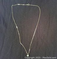 Full view of necklace with chain and pendant against black fabric background.