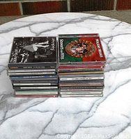 Two stacks of various artist music CDs on a marble-like surface showing album covers and spines.