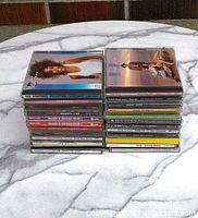 Two stacks of CDs featuring multiple artist albums including Whitney Houston and Rod Stewart