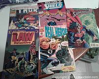 Five comic books laid out showing front covers with varying titles including Marvel's Real Heroes, Nick Fury, Hulk; DC's Superman; and Classic Comics' John Law Detective.