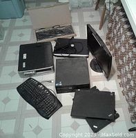 View of all items including 2 desktops, 3 laptops, large monitor, keyboards, and cables arranged on tiled floor