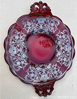 Top view of cranberry glass plate with detailed silver overlay floral and urn design around the rim and decorative handles