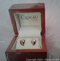 Pair of heart-shaped rose gold earrings in a wooden box with Clogau Gold branding inside lid.