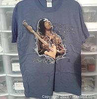 Front view of slate color Jimi Hendrix t-shirt with graphic of Hendrix playing guitar and text 'The Story'.