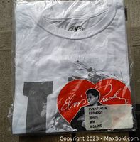 Photo of the packaged t-shirt showing part of the white shirt with a partial graphic of Elvis Presley and a red heart with signature, with a sticker showing size M and product codes.
