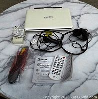 Closed Toshiba portable DVD/CD player with top visible, surrounded by cables, remote, and manual on marble surface.