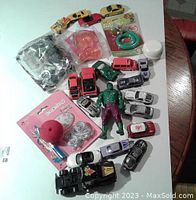 Top view of toy lot showing 11 miniature cars, Hulk action figure, party accessory pack, black toy truck, and sealed packs