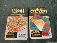 Full view of two metal tins with colorful printed lids for Snakes & Ladders and Chinese Checkers games