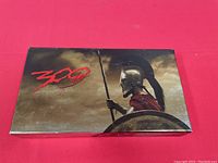 Front view of outer slipcover featuring Spartan warrior in armor with spear and shield under red 300 logo on gold background.