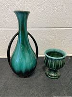Full view of the two ceramic Green Blue Mountain Pottery pieces on a black textured surface against a plain white wall.