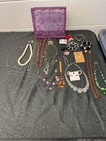 Full view of assorted costume jewellery including necklaces, bracelets, earrings, and decorative box on grey fabric.