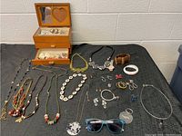 Full view of costume jewelry lot with necklaces, rings, earrings, bracelet, sunglasses, and wooden jewelry box