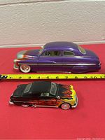 Side view of two diecast model cars showing size and detail, purple 1949 Mercury Led Sled Coupe and black flame decal car