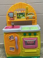 Front view of Dora the Explorer talking kitchen showing sink, stove, oven, refrigerator with Dora stickers, and top arch with screen and blender accessory