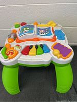 Top-down view of LeapFrog toddler play table showing all interactive features clearly including piano keys, xylophone, spinning elements, and open book design.