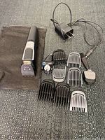 Full view of shaver set showing main unit, charger, six comb attachments, two detachable heads and pouch on fabric surface