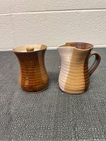 View of both pottery pieces: a creamer and a lidded sugar container on a textured dark surface with a beige background.
