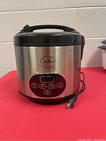 Front view of Crofton rice cooker showing stainless steel body, black lid and control panel with buttons and display.