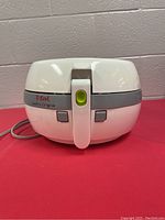 Front view of white T-fal ActiFry Original air fryer with handle and green release button, power cord visible on side.
