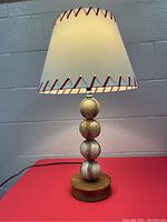 Full view of the baseball lamp showing the shade with red baseball stitch design and the four stacked baseballs on a wooden base.