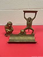 Three brass monkey desk items on a red surface against a white brick wall